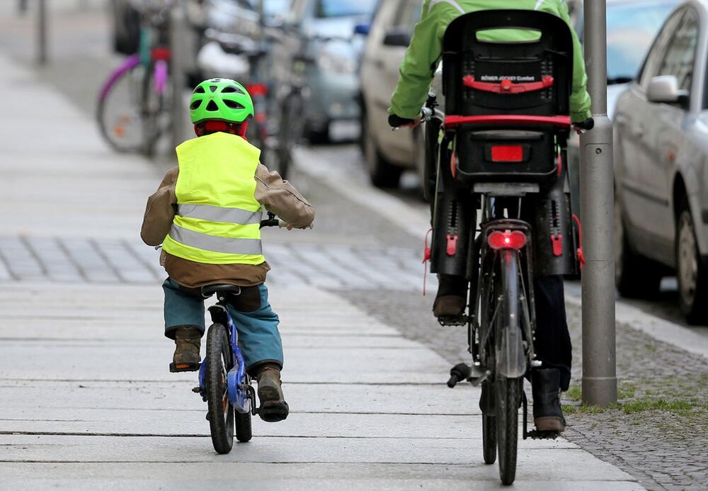 Ein Kind fährt mit dem Rad auf dem Fußweg neben einem Elternteil