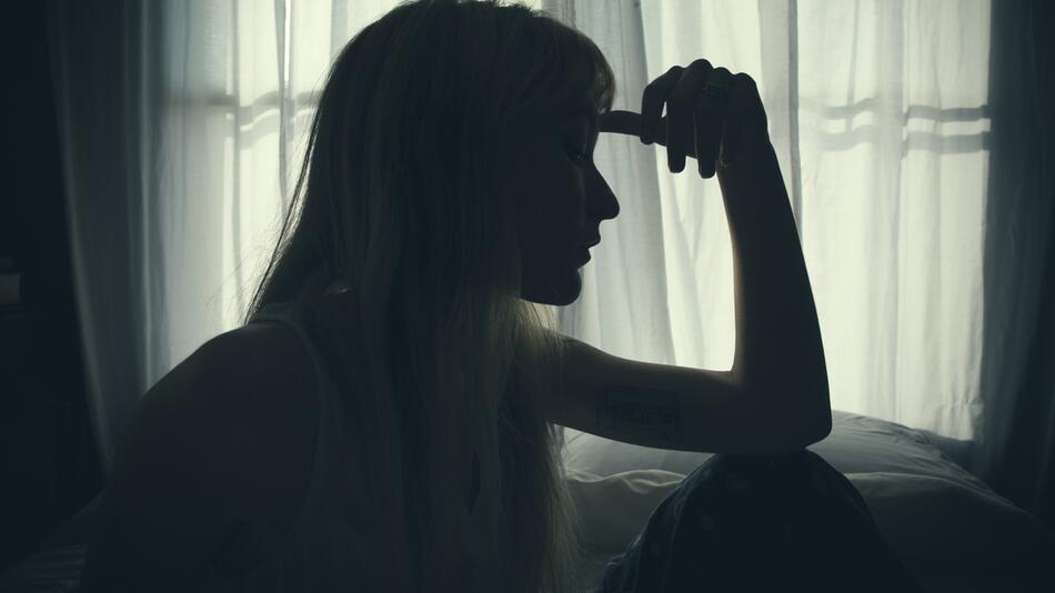 Eine junge Frau liegt mit erschöpftem Gesichtsausdruck bewegungslos im Bett.