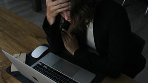 Eine Frau sitzt an einem Holztisch vor einem geöffneten Laptop, hält sich mit einer Hand den ...