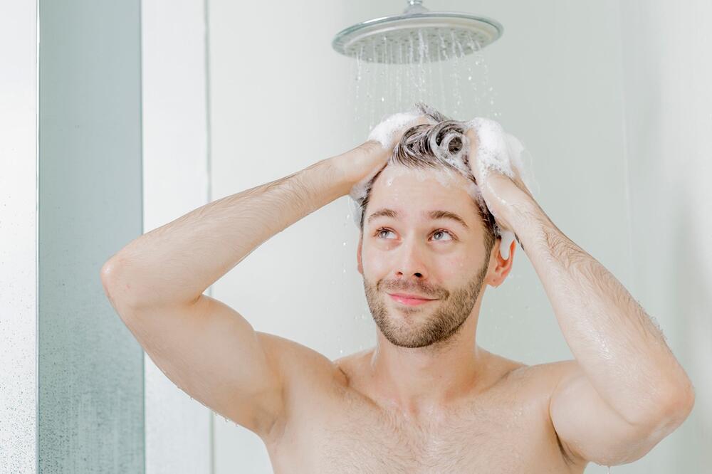 Mann wäscht sich unter der Dusche die Haare