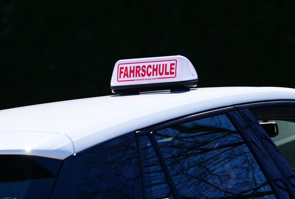 Schild "Fahrschule" ist auf einem Fahrschulauto befestigt