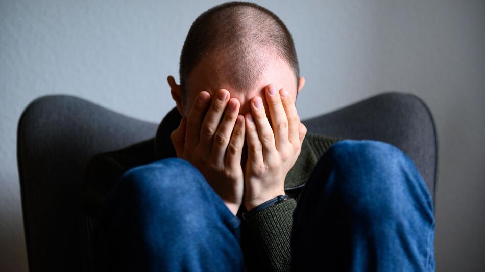 Ein Mann sitzt mit Händen vor dem Gesicht zusammengekauert auf einem Stuhl. (gestellte Szene)