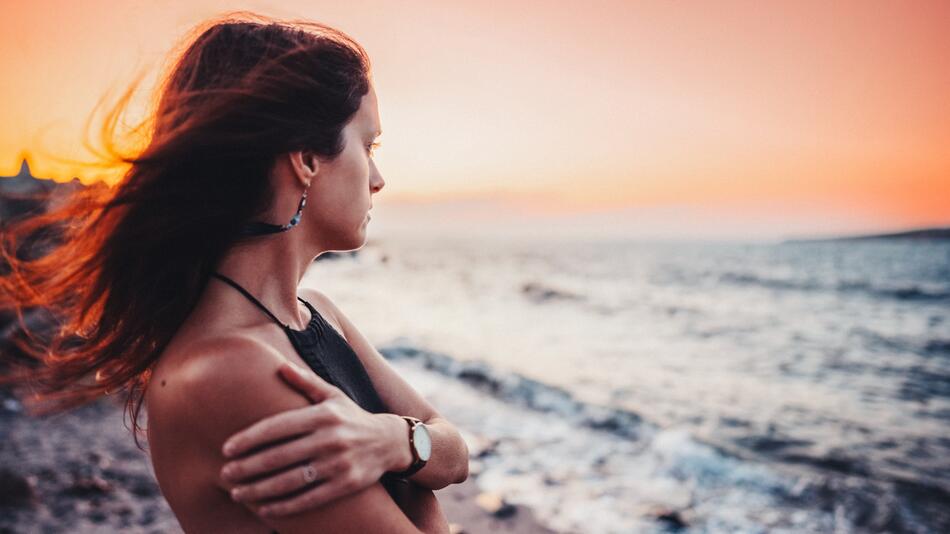 Frau schaut traurig aufs Meer