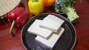 Drei Scheiben Tofu auf einem schwarzen Teller, umgeben von roter, gelber und oranger Paprika ...
