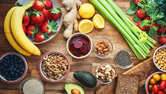 Gesunde Lebensmittel wie Obst, Gemüse, Nüsse und Hülsenfrüchte in Schüsseln