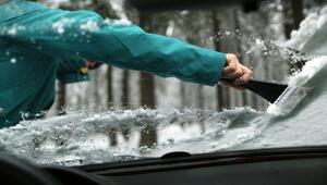 Ein Mann kratzt die verschneiten Scheiben eines Autos frei