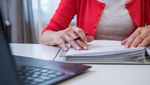 Eine ältere Frau arbeitet mit Unterlagen am Laptop