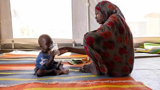 Eine Mutter gibt ihrem Kind einen Becher mit Flüssigkeit