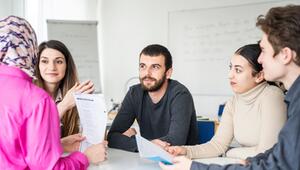 Fünf Erwachsene sitzen um einen Tisch in einem Klassenraum