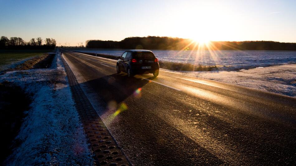 Auto fährt bei Sonnenaufgang über eine spiegelglatte Landstraße