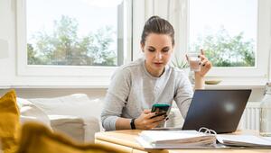 Eine Frau tippt auf einem Smartphone vor einem Laptop