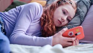 Foto eines melancholischen Teenager-Mädchens, das auf dem Bett liegt und auf ein Smartphone starrt