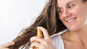 Eine Frau sprüht sich mit einem Haarpflegeprodukt auf die Haare