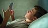 Ein Jugendlicher liegt einsam im Bett und starrt auf sein Smartphone