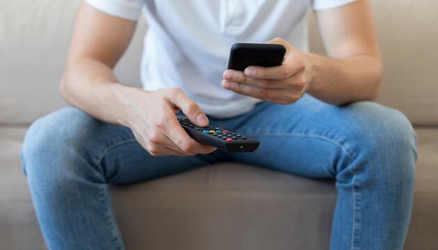 Mann mit Fernbedienung und Smartphone in der Hand