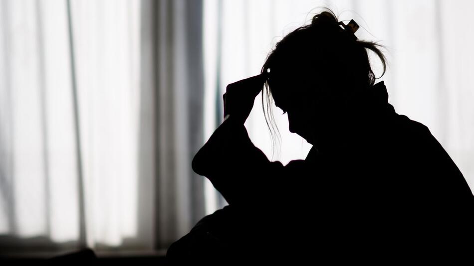 Die Silhouette einer Frau zeichnet sich vor einer hellen Fensterfront ab