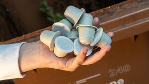 Frau hält kompostierbare Kaffeekapseln vor einer Bio-Mülltonne