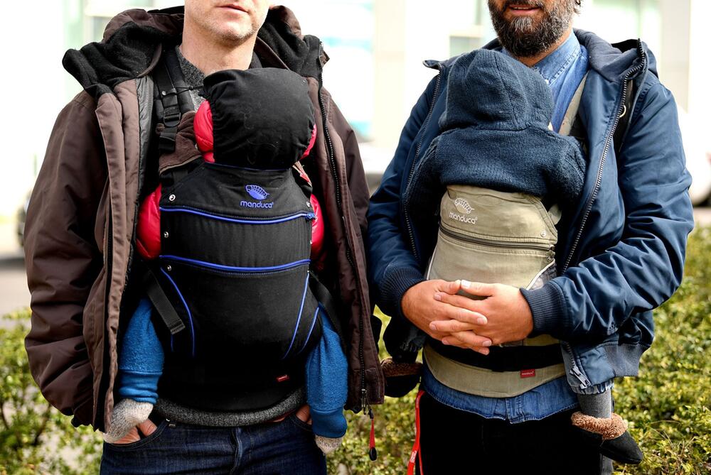 Zwei Männer tragen ihre Kinder in Kindertragen