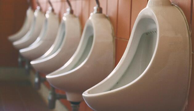 Pissoirs an einer orangen Fliesenwand. 