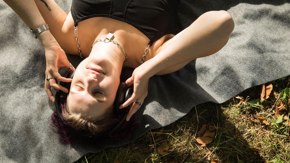 Eine diverse Person mit Kopfhörern im Park