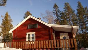 Rotes Holzhaus mit weißem Fensterrahmen und Tür, Solarzelle an der Hauswand, umgeben von ...