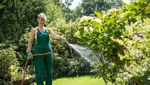 Eine Frau gießt Pflanzen mit einem Gartenschlauch