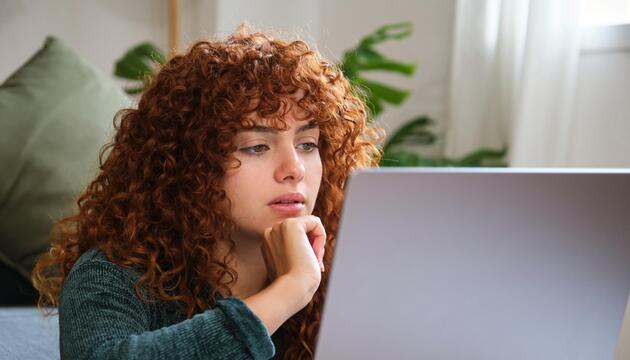 Junge Frau mit roten Locken, die vor Laptop sitzt. 