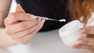 Eine Frau entnimmt mit einem Spatel Creme aus einem Tiegel