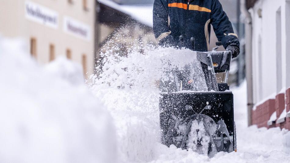 Ein Mann beräumt den Gehweg mit einer Schneefräse