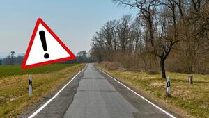 Eine schmale Landstraße mit unebener, reparierter Asphaltoberfläche, umgeben von Wiesen und ...