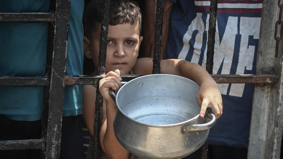 Foto eines Kindes mit leerem Topf in Gaza-Stadt, das auf Essen von Hilfsorganisationen wartet