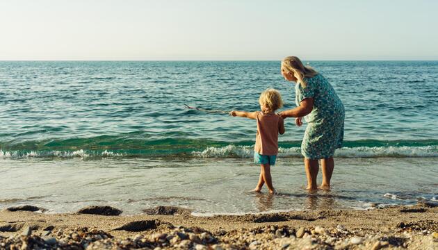 Ältere Frau und Kind schauen vom Strand aus aufs Meer