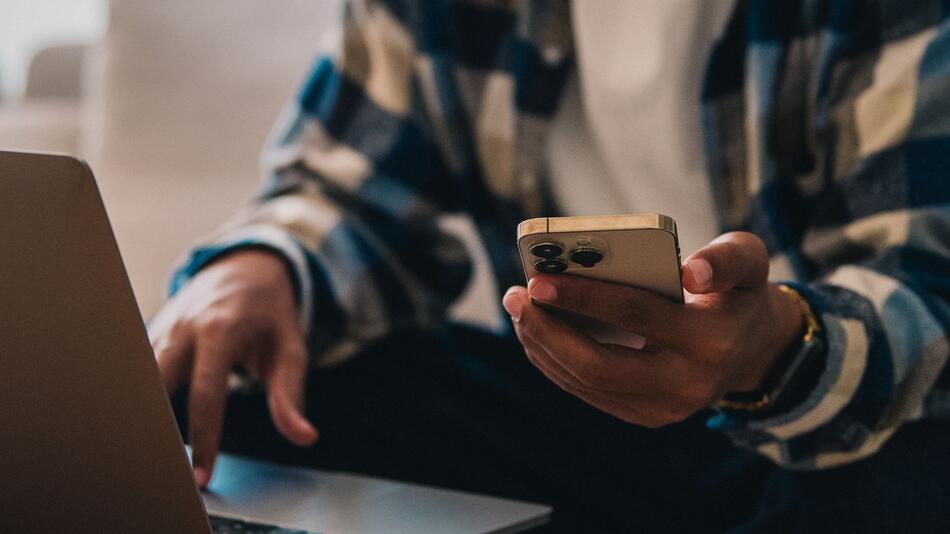 Ein Mann arbeitet am Laptop und hält ein Smartphone in der Hand