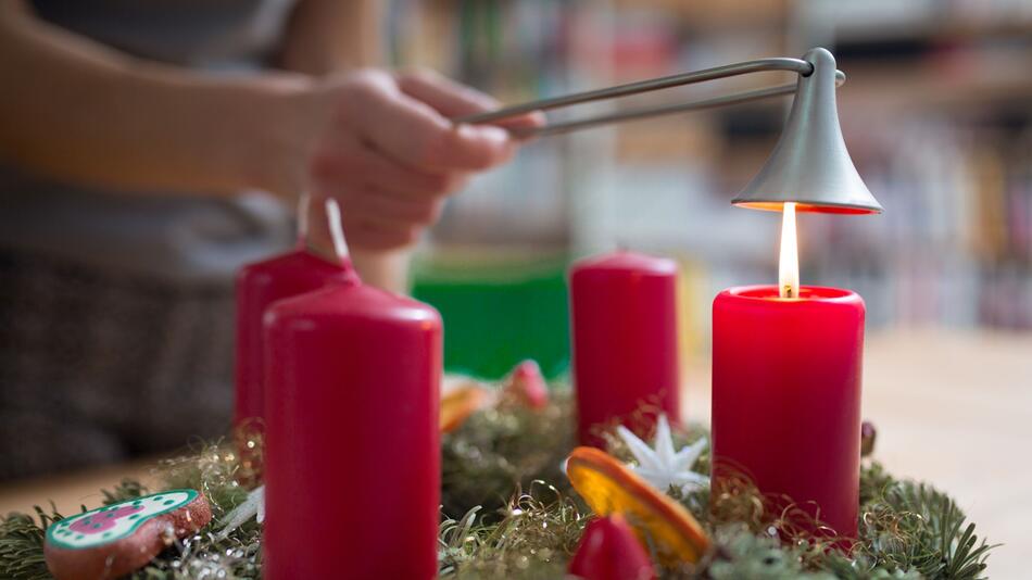 Frau löscht eine Kerze an einem Adventskranz