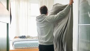 Ein Mann bezieht das Bett und schüttelt dabei eine Bettdecke