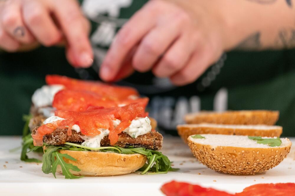 Eine Köchin belegt einen Burger mit veganem Fischersatz