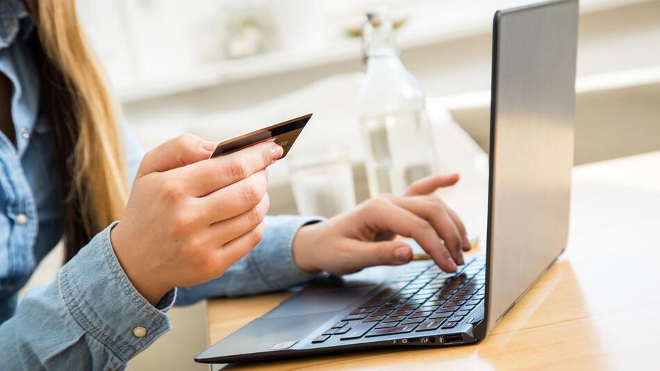 Frau sitzt mit einer Kreditkarte vor einem Laptop