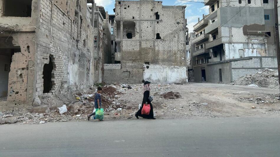 Eine Frau und ihr Kind laufen vor zertrümmerten Häusern in Homs