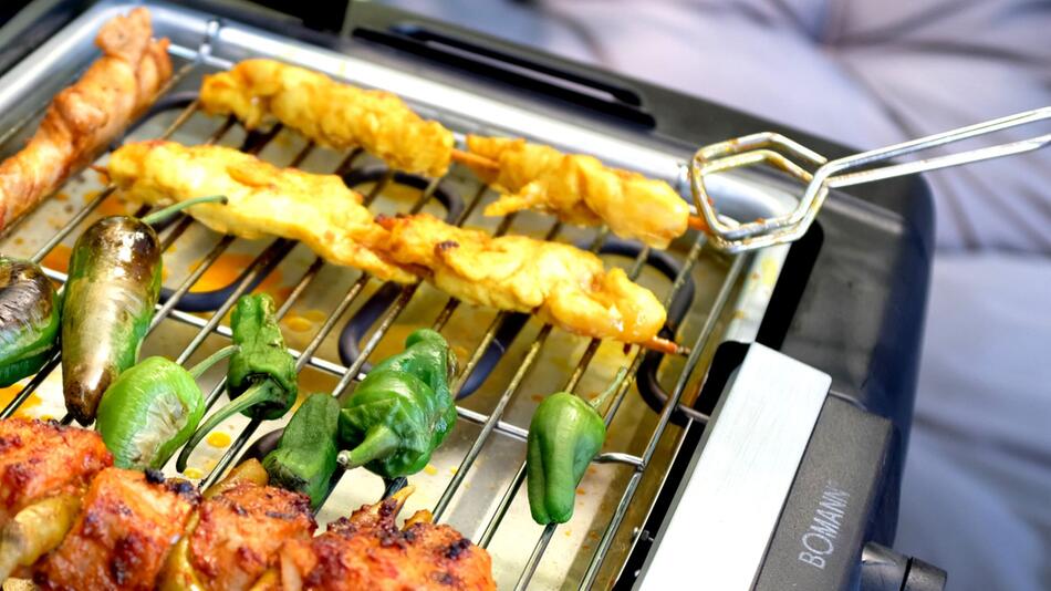 Ein Mann grillt mit einem Elektrogrill auf einem Balkon