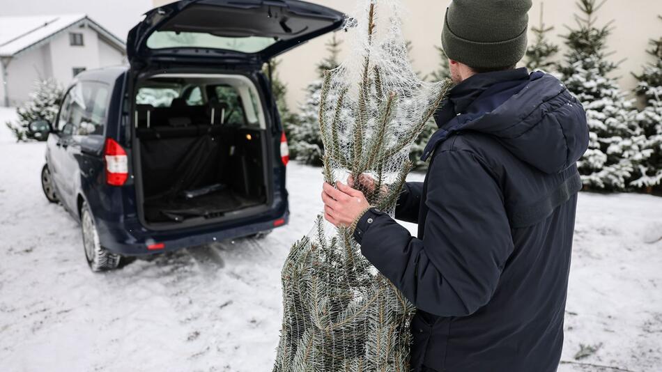 Ein Mann steht mit einem Weihnachtsbaum vor seinem Wagen