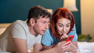 Eine Frau und ein Mann liegen auf dem Bett und schauen gespannt auf das Smartphone.