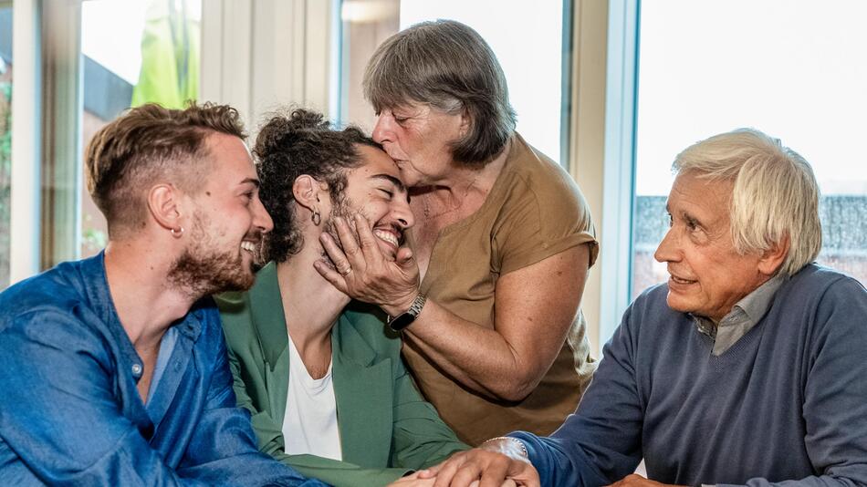 Queeres Paar outet sich vor Großeltern, die mit Umarmungen und Küssen reagieren.