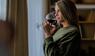Frau steht am Fenster und trinkt ein Glas Rotwein