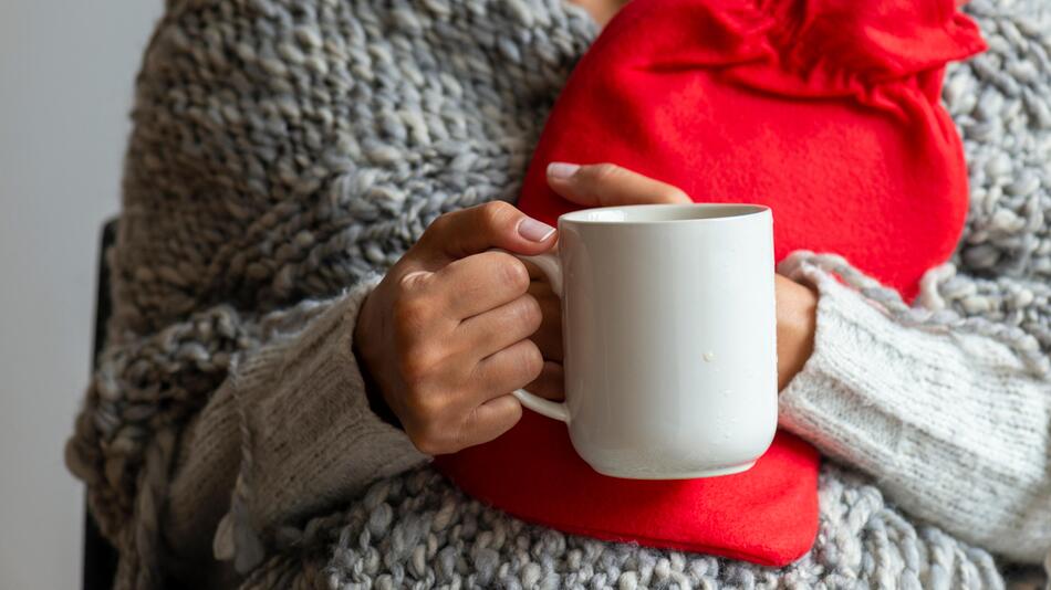 Frau hält Wärmflasche und Tasse Tee in der Hand