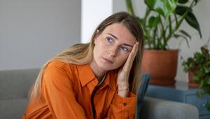Eine Frau sitzt nachdenklich auf einem grauen Sofa.