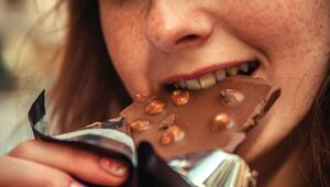 Nahaufnahme eines Gesichts mit Sommersprossen, das in eine Schokoladentafel mit ganzen ...