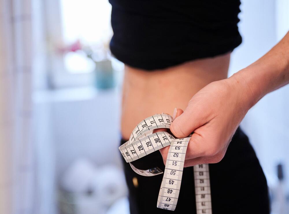 Eine junge Frau hält ein Zentimetermaßband an ihren Bauch