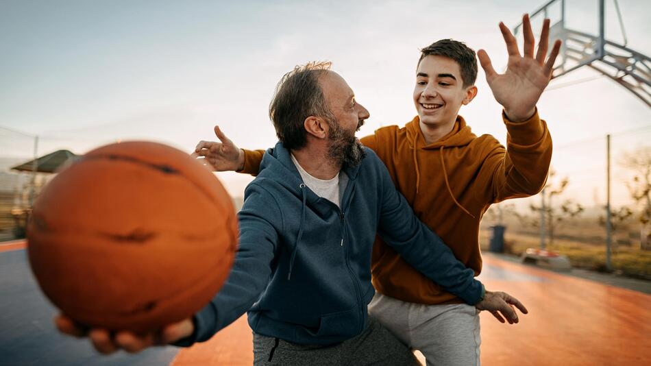 Älterer Mann und Junge spielen Basketball