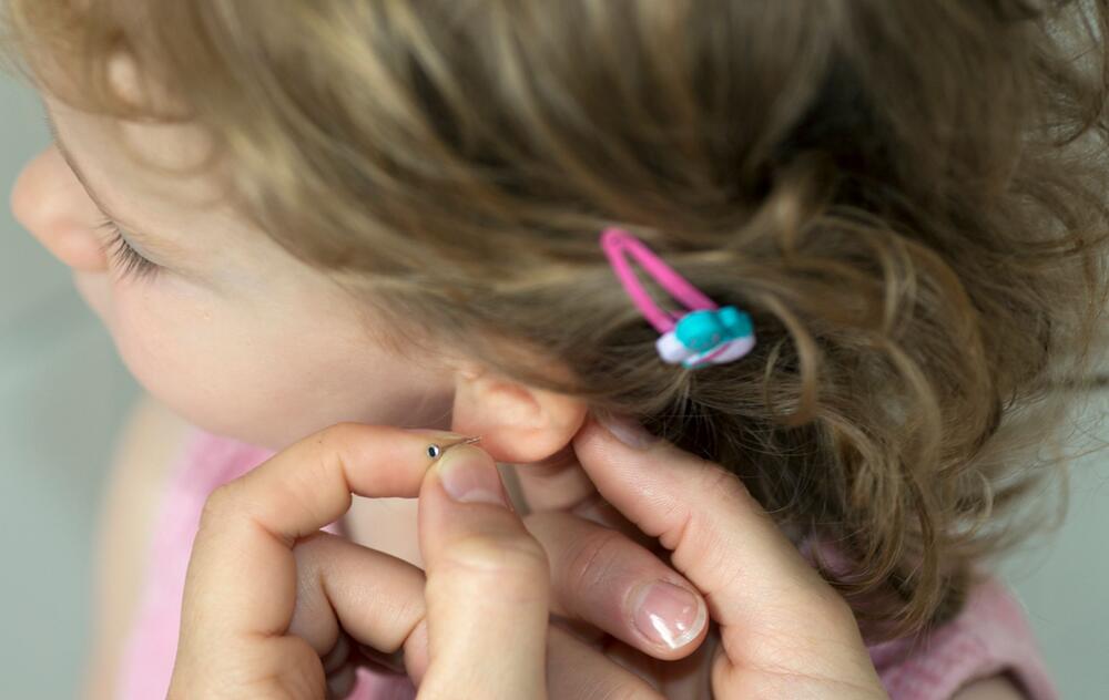 Mutter hält Ohrstecker an das Ohrläppchen ihrer Tochter