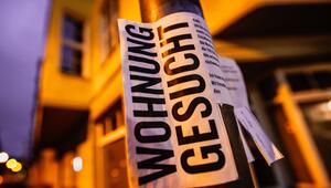 Ein Zettel mit der Aufschrift "Wohnung gesucht" vor Wohnhäusern